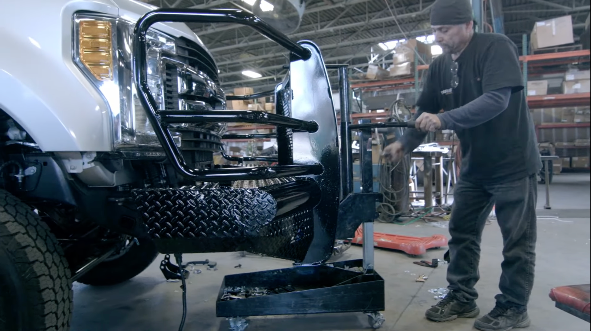 Use a hydraulic lift to raise the bumper into place and align it with the truck